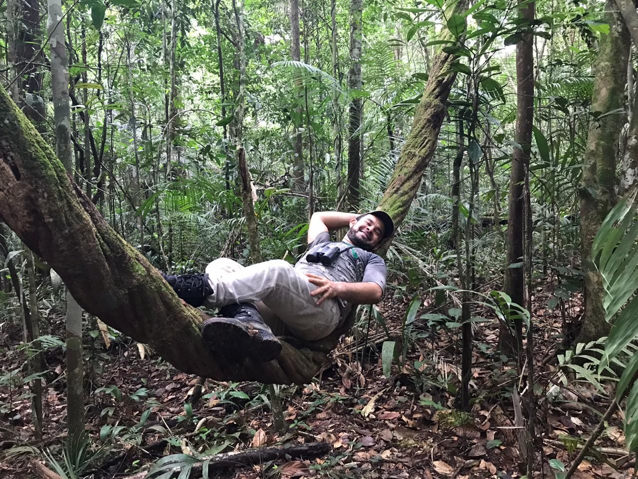 Naturalist guide resting on a giant tree root during a primary jungle walk in the Amazon rainforest